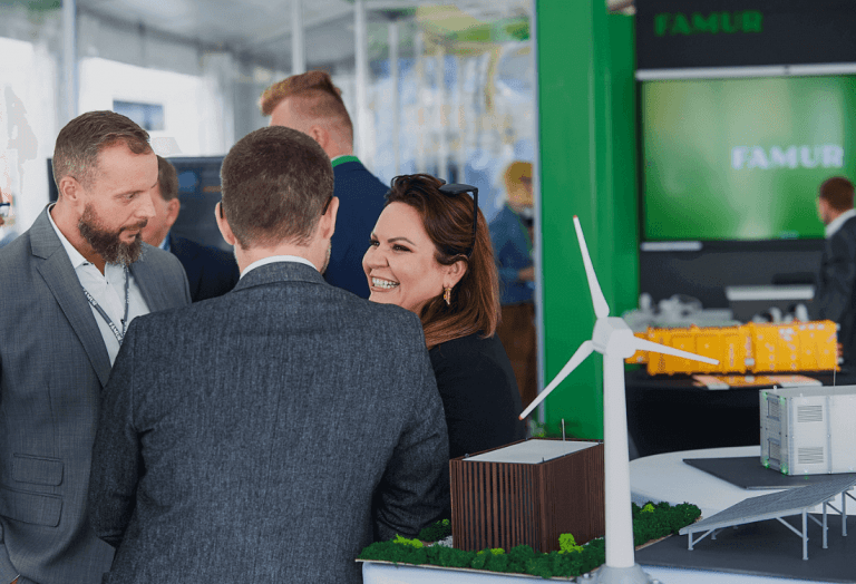 Na pierwszym planie w prawym roku znajduje się model farmy wiatrowej a za nią w tle widać uśmiechniętą od ucha do ucha Martę Rzepecką, która omawia z potencjalnymi inwestorami możliwość współpracy z Projekt Solartechnik w kontekście działań b2b.